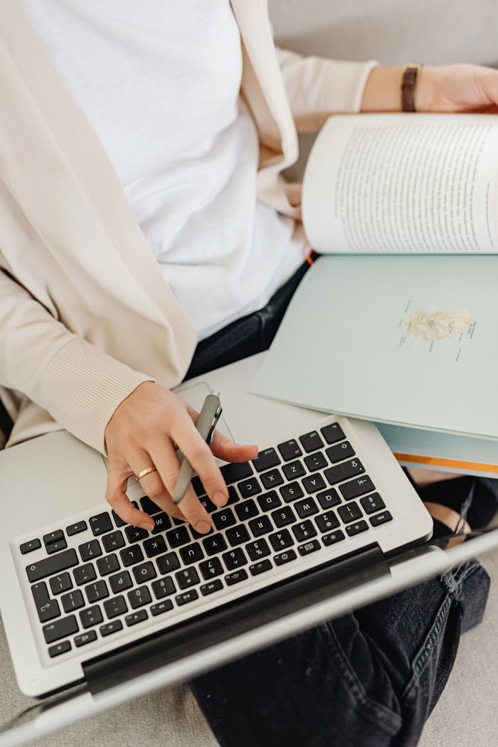 contact-header Close-up of a person multitasking with a laptop and a book, emphasizing productivity and casual work.